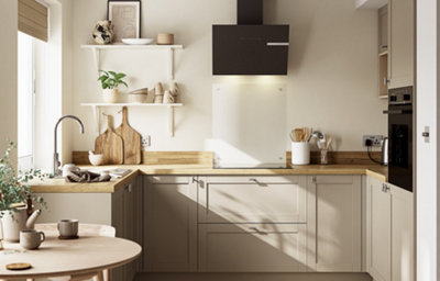 Modern U-shaped kitchen with pebble-coloured shaker-style cabinets, light wood worktops and a black angled cooker hood. Open white shelves display plants, pottery and decorative bowls, while wooden chopping boards rest against the backsplash