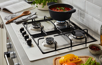 Close-up of ivory kitchen cabinets, gas burner chrome and black hob, and grey worktop.
