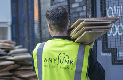 back of man with anyjunk hi viz yellow vest carrying a stack of wood