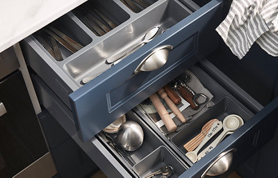 Two shaker style kitchen drawers in a dark blue shade and a matt finish have been opened to reveal cutlery and various kitchen utensils.