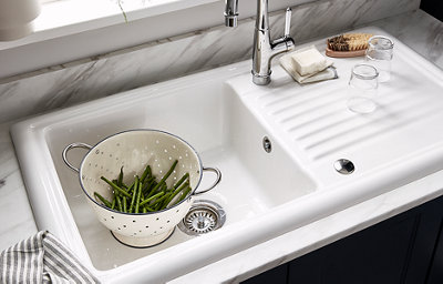 A glossy white kitchen sink and stainless steel hardware gleam in the light. In the sink, green beans are draining in a colander.