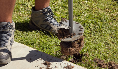 Person spinning an auger into the ground next to a patio to create a hole.