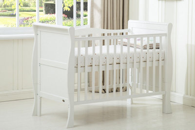 A white cot with curved details, in a bright nursery.
