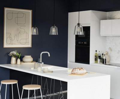Three glass domed pendant lights with black cords hanging over a kitchen island in a white and blue kitchen.
