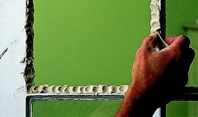 Person using their thumb to press putty into the edge of a window frame, preparing it for the installation of a new pane of glass.