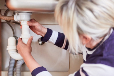 Person unscrewing the connector that joins the kitchen sink waste to the kitchen sink by hand.