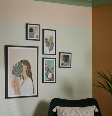 Selection of mixed side framed botanical art prints on the wall besides an armchair.