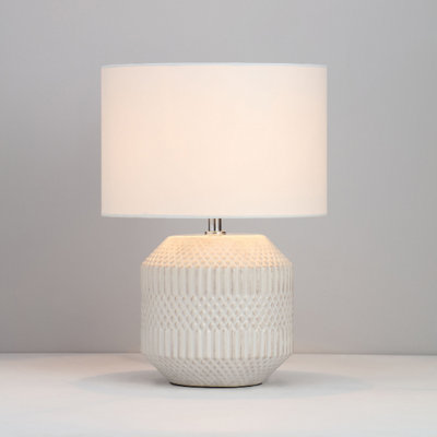 White table lamp with ceramic base with an embossed design and white shade.