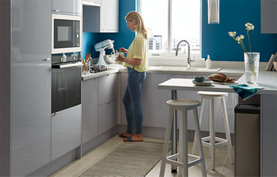 Gloss grey kitchen with white worktops and bold blue walls. Includes a compact breakfast bar with stools, integrated appliances, and modern accessories. 4/4