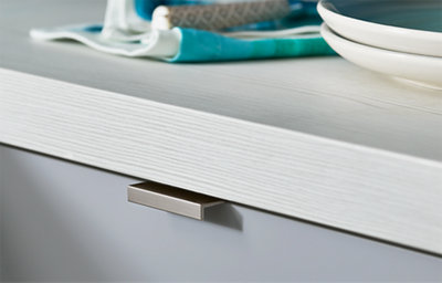 Close-up of a textured white wood-effect worktop with modern brushed metal handle and stacked plates.