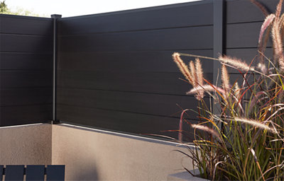 The Neva fence panel range ,showing the dark grey fence slats, installed above a short garden wall. 