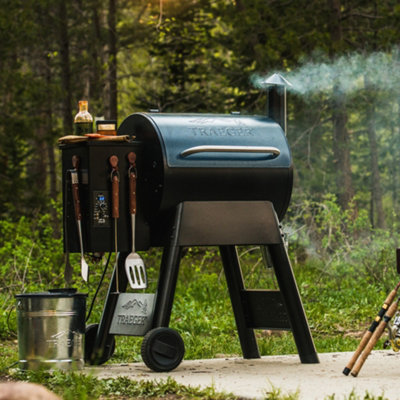 Traeger wood-pellet grill barbecue with lid closed in a forest setting.