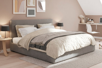 Beige bedroom with light wood effect laminate flooring, a light grey upholstered bed, and abstract gallery wall above headboard.