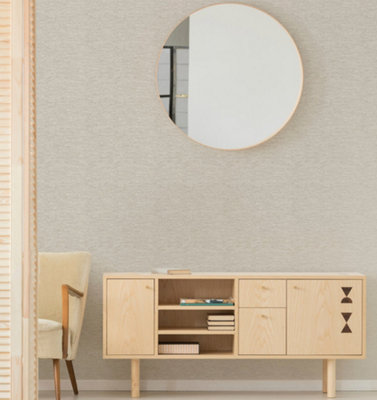 Light grey textured wallpaper in a room with a light wooden sideboard and and a large circular wall-mounted mirror.
