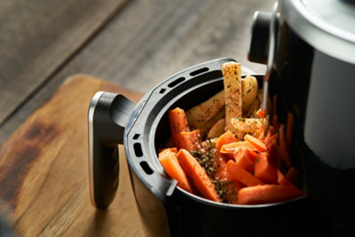 An air fryer sitting on a kitchen worktop with the drawer open, showing vegetables cooking inside.