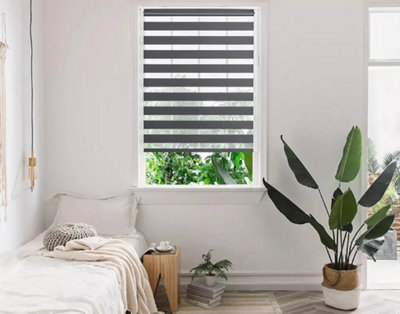 Grey blinds installed in a tall window in a minimalist bedroom.
