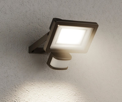 A black security light with a motion sensor on the bottom, installed on a wall.