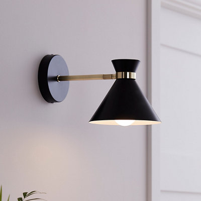 A kitchen wall light with a black shade, attached to a wall fixing by a gold-coloured bar.