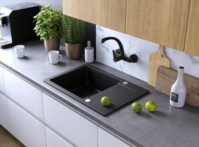 A black wall mounted kitchen tap attached to a marble effect splashback.