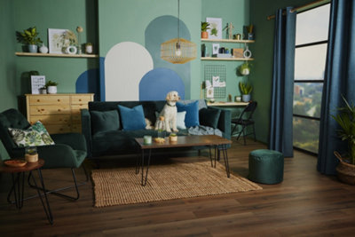 Blue and green curved wall mural behind a deep green sofa in in green living room.
