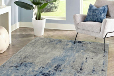 A blue abstract statement rug in a living room with light wooden flooring and a cream fabric armchair.