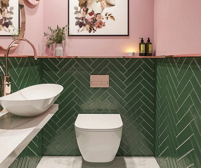 Small cloakroom bathroom with green herringbone tiles on the bottom half of the wall and a bold pink paint on the top half.