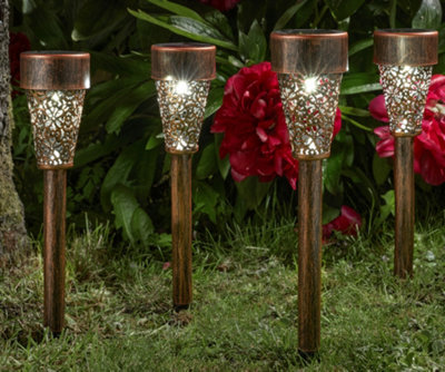 Four small stake lights with a copper finish, installed in the grass in front of a flower bed.