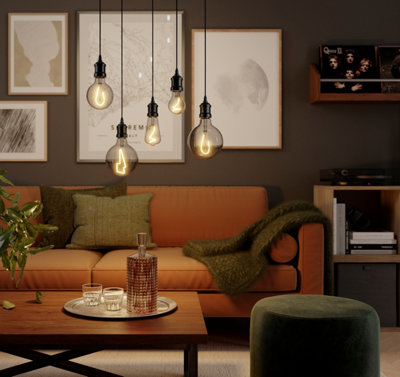 A brown living room with a tan leather sofa, gallery wall, and industrial-style exposed bulbs.