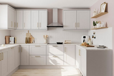 A white kitchen with white cabinetry, rose gold effect handles, pale pink walls and light wooden flooring.