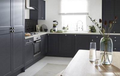 Shaker style kitchen cabinets in dark grey with a matt finish are finished with silver coloured door knobs. On the white worktop sits a fixed cabinet with a top-hinge opening.