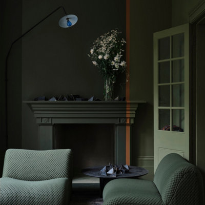 A cosy living room with deep green walls, a lighter green section divided by a thin orange-brown stripe, and a painted fireplace for added texture.