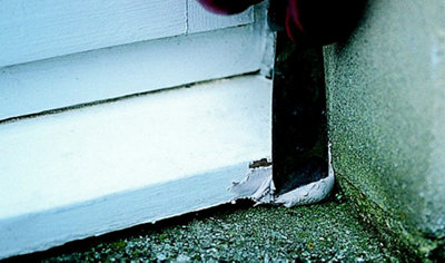 Person using a narrow-bladed scraper to push wood filler into the corner of a timber windowsill.