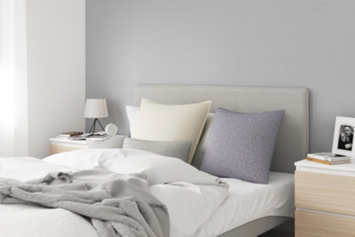 A minimalist bedroom with light grey walls, a white bed, and light wooden side tables either side of the bed.