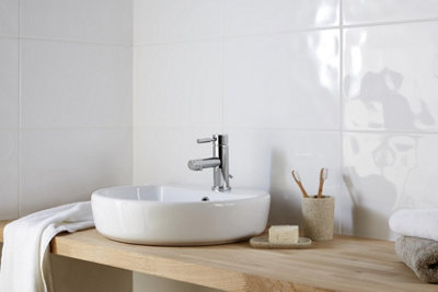 White bathroom tiles behind a wooden vanity unit with a white countertop basin.