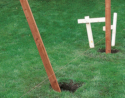 Two fence posts positioned in holes in the ground, with a builder's line stretched between them.
