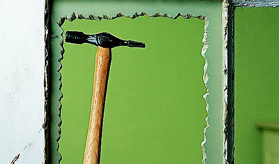 Person using a hammer to secure a glazing panel pin into the edge of a window frame, fixing the glass in place.