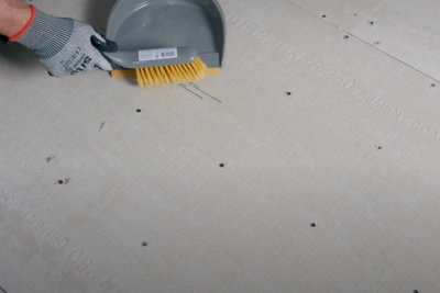 Person using a dustpan and brush to clean a bathroom floor with tile backer boards installed on top.