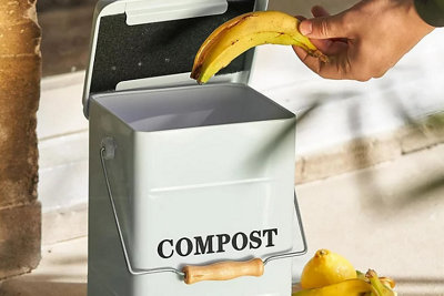 Person placing a banana peel into a small metal bin with a handle labelled compost.