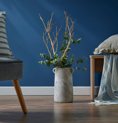 Concrete floor vase full of twigs and dried eucalyptus in a blue living room.
