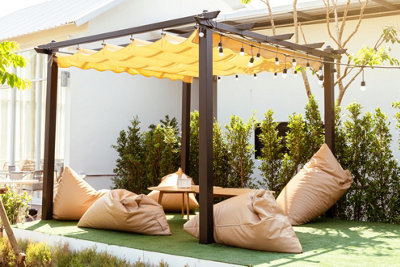 An inviting garden setup within a dark wooden pergola, featuring outdoor bean bags around a low coffee table, creating a cosy and relaxed space.