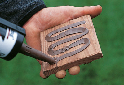 Person using a sealant gun to apply sealant to the bottom of a timber fence post cap.