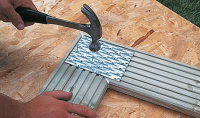 Person using a hammer and nails to join two decking boards in a corner with a metal plate.