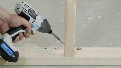 Driving a wood screw downwards at an angle into a vertical stud to secure it to the floor plate.