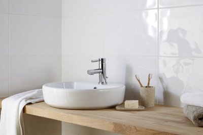 A white bathroom with gloss white wall tiles and a small white basin mounted on a wooden worktop.