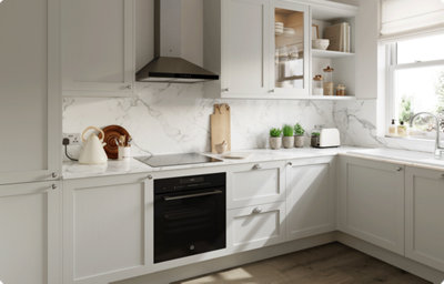A shaker-style kitchen in light grey is bathed in light from a nearby window. The matt finish creates a uniform look whether the cabinets are in light or shade. The white and grey marble-effect countertop extends to create a striking splashback around the L-shaped kitchen.