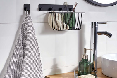 Hooks installed on bathroom tiles, with one hook holding a towel and another set of four hooks supporting a metal basket containing toothbrushes and a flannel.