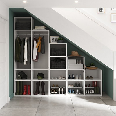 A shelving unit built under the sloping ceiling beneath a staircase, featuring a coat rack and multiple square cubby holes storing shoes and other accessories.