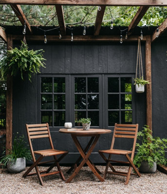 A dark wooden pergola adorned with twinkling string lights and hanging plants, standing against black external walls.