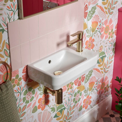 Small white wall hung basin in a pink bathroom with a pale pink tiled splashback and floral wallpaper.