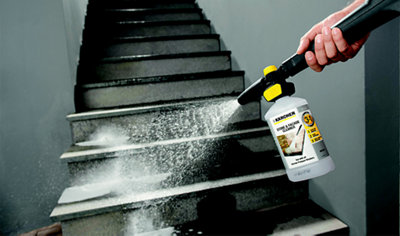 Person using a pressure washer detergent tank to spray detergent onto concrete steps.